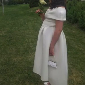 Vit offshoulder långklänning - Elegant vit långklänning med offshoulder-design och markerad midja. Klänningen har en stilren och klassisk siluett med lätt utställd kjol, perfekt för speciella tillfällen. Och den är mjuk i tiget.