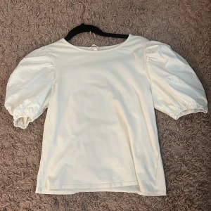 Vit topp med puffärmar - Säljer en stilren vit topp med puffiga kortärmar och rund halsringning. Toppen har en mjuk och slät yta som ger en elegant känsla. Perfekt för dig som gillar en enkel men trendig look.