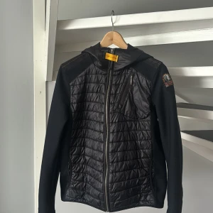 Svart jacka med huva från Parajumpers - Snygg svart jacka från Parajumpers med innerfickor och huva. Jackan har dragkedja framtill, bröstficka med dragkedja. Den är i väldigt fint skick så bara att höra av dig om du undrar över något! Och såklart 100% äkta 