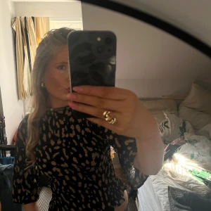 Mönster blus  - Trendig topp med svart botten och beige/brun mönster. Hög hals och trekvartsärmar, smockad midja som ger en snygg siluett. Perfekt till jeans eller kjol för en cool look.