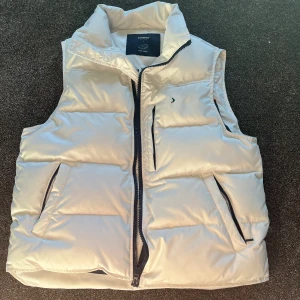Boomerang dunväst – Storlek L - Säljer en stilren och varm dunväst från Boomerang i storlek L. Modellen heter Microft Down Vest och är gjord i äkta dun (pure down), vilket gör den perfekt för kyliga dagar. Färg: vit med mörkblå detaljer och röd piping på insidan. Detaljer: 	•	Två sidofickor med dragkedja 	•	En bröstficka med dragkedja 	•	Broderad Boomerang-logga på bröstet och nacken 	•	Innerfoder i marinblått 	•	Väldigt bra skick, använd typ 2 gånger Nypris ligger vanligtvis runt 1 500–2 000 kr. Pris kan diskuteras