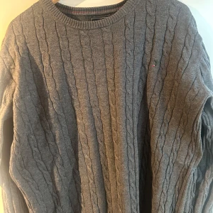 Grå kabelstickad tröja från Boomerang - Säljer en klassisk grå kabelstickad tröja från Boomerang i storlek L. Tröjan har rund halsringning, lång ärm och diskret broderad logga på bröstet. Perfekt för lager-på-lager och passar till många olika stilar.