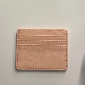 Beige kortfodral i skinn - Säljer ett oanvänt, stilrent och smidigt kortfodral i rosa färg. Perfekt för dig som vill ha koll på dina kort utan att ta plats. Fodralet har flera fack för kort och är lätt att bära med sig i fickan eller väskan.
