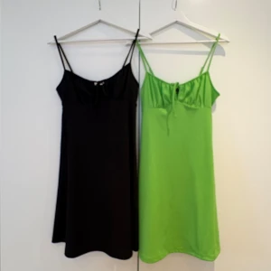 Svart och grön klänning med smala axelband - Två stilrena klänningar med smala axelband, en i svart och en i klargrön. Båda har en enkel, rak passform och liten rosettdetalj framtill. Perfekta för sommardagar eller sommarfester.