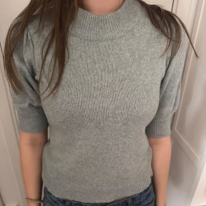 Ljusgrön stickad tröja med halvlånga ärmar - Säljer en ljusgrön stickad tröja med halvlånga ärmar och hög ribbad hals. Tröjan har en klassisk, enkel design och är mjuk och bekväm. Perfekt till jeans eller kjol för en stilren look.