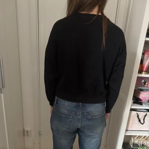 Svart Stranger Things sweatshirt - Säljer en svart sweatshirt med Stranger Things-logga i blått och rött framtill. Tröjan har rund halsringning och långa ärmar. Perfekt för dig som gillar serien och vill ha en bekväm och stilren tröja.