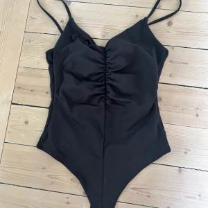 Svart body från H&M - Säljer en svart body från H&M med smala axelband och rynkdetalj framtill. Toppen har en tight passform och är perfekt att styla med jeans eller kjol.