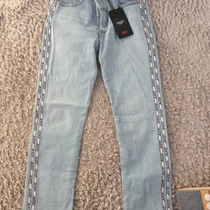 Levi's 501 Cropped jeans med logoband - Ljusblå Levi's 501 Cropped jeans med raka ben och vita logoband längs sidorna. Aldrig använda. STORLEKEN ÄR: 28 X 28 !!! levi’s storlek. Jätte fina men inte min stil