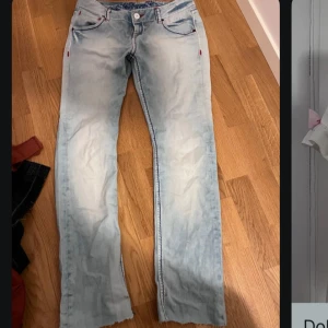 Ljusblå lågmidjade bootcut jeans från Miss Sixty - Säljer ett par ljusblå jeansbyxor från Miss Sixty med lätt utsvängda ben och snygga röda sömdetaljer. Byxorna har broderad logga i midjan och klassiska fem fickor. Perfekta för dig som gillar unik denimstil! Lågmidjad, vintage, jättesnyggt!! Passar typ S/M. Klippta där nere så de passar till folk som är 165-170cm ungefär