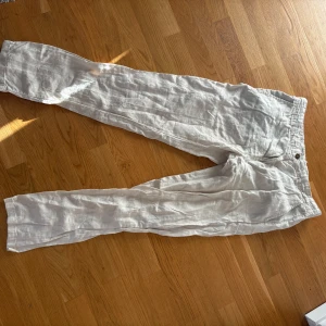 Beiga linnebyxor från Kaporal - Snygga och luftiga beiga linnebyxor från Kaporal med klassisk passform. Byxorna har dragkedja och knapp framtill samt bälteshällor. Perfekta för varma dagar och en avslappnad stil.