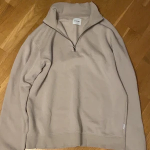 Beige halvzip tröja från Jack & Jones - Säljer en beige långärmad halvzip tröja från Jack & Jones. Tröjan har hög krage och dragkedja framtill, perfekt för lager-på-lager. Mjuk och skön, passar till många tillfällen.