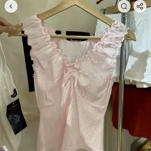 Ljusrosa ribbad linnetopp med volang och rosett - Supersöt ljusrosa linnetopp från brandy Melville, volangkant vid axlar och urringning och rosett framtill. Storlek S har prislapp kvar och aldrig använts 