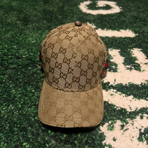 Beige keps med GG mönster  - Säljer en beige keps med klassiskt GG-monogram över hela kepsen och en röd-grön rand på sidan. Justerbar rem baktill och svart insidan. Perfekt för dig som gillar exklusiva accessoarer. Vid funderingar skriv!! Vid snabb affär bättre💸