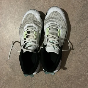 Basket Nike skor - Säljer ett par Nike sneakers i vitt, svart och mintgrönt. Skorna har snörning, vågig sula och en stor svart swoosh på sidan. Ovandelen är i mesh med mintgröna detaljer och vit bas. Perfekta för träning eller vardag.