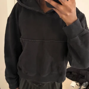 Svart hoodie med huva - Säljer en svart hoodie med huva och magficka. Tröjan har en avslappnad passform och ribbade muddar vid ärmslut och nederkant. Perfekt för en chill och bekväm stil.