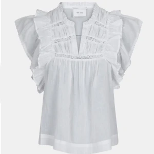 Vit blus med volang och spetsdetaljer - Superfin vit blus med volangdetaljer på axlarna och spetsinslag framtill. Blusen har en lös passform och är tillverkad i ett lätt bomullstyg, perfekt för varma dagar. Djup v-ringning och korta ärmar ger en luftig känsla. Inga tecken på användning då den inte använts mer än två gånger, som helt ny. 