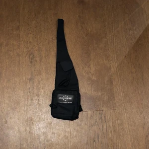 Svart axelväska från Chronostar - Säljer en svart axelväska från Chronostar med justerbar rem och praktiskt fack framtill. Enkel och stilren design med logga på framsidan.