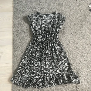 Svartvit blommig klänning från XOXO Friends - Söt svart klänning med vitt blommönster från XOXO Friends. Klänningen har korta ärmar, resår i midjan och volangkant nertill. Perfekt för sommaren, midsommar och skolavslutningen 💕