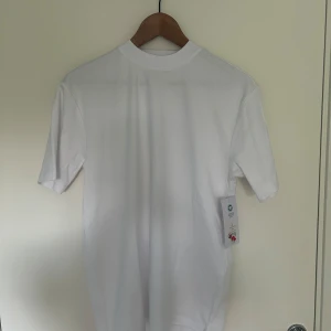 Vit t-shirt från S.C.W. - Klassisk vit t-shirt från S.C.W. med rund hals och normal passform. Perfekt basplagg i garderoben, tillverkad i mjuk bomull för en skön känsla. Enkel och stilren design utan tryck eller mönster. Helt oanvänd, prislappen sitter kvar!