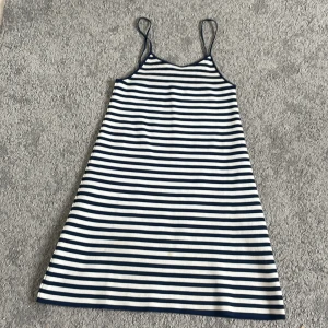Randig sommarklänning från MNG - Säljer en vit och marinblå randig klänning från MNG med smala axelband. Klänningen är ärmlös och har en avslappnad passform, perfekt för varma dagar. Mjuk bomullskänsla och klassiskt mönster.