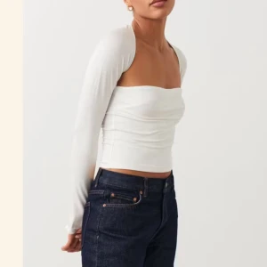 Vit croppad bolerotopp - Trendig vit croppad bolerotopp med långa ärmar och axelbandslös design. Perfekt för att skapa en stilren och modern look. Snygg att matcha med jeans eller kjol.