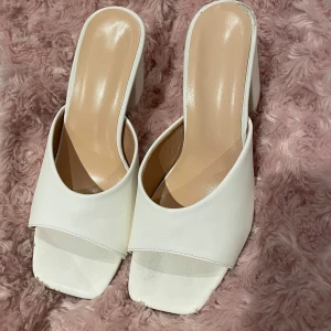 Vita slip-in klackar med fyrkantig tå - Storlek 37. Säljer ett par stilrena vita slip-in klackar med block-klack. Använt skorna en gång därav lite slit på undersidan och hälen. Perfekta för balen, jättebekväma och lätta att gå i!💗