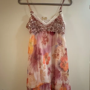 Ibiza klänning  - Säljer en romantisk klänning från Exex med glittrig paljettliv i rosa och smala axelband. Kjolen är blommig i rosa, lila och orange toner med lätt och luftig känsla. Perfekt för sommarens alla tillfällen!