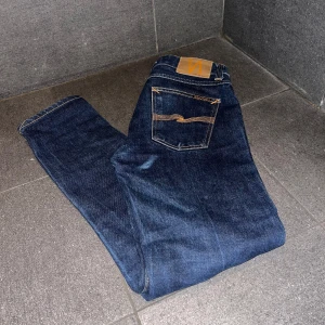 Dry Japan selvage nudie jeans - Säljer ett par mörkblå jeans från Nudie Jeans med klassiska orange sömmar och snygga bakfickor med vågig detalj. Nypris 2500. Jeansen är lean dean. Det är japanska selvage jeans i riktigt bra skick och bra kvalité.