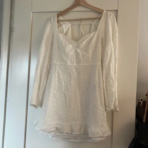 Vit sommarklänning  - Superfin vit klänning med broderade blommor, v-ringning och volang nertill. Långa puffärmar och öppen rygg med knytband. Perfekt för sommarens alla tillfällen!