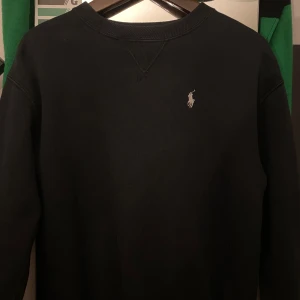 Svart sweatshirt från Polo Ralph Lauren - Klassisk svart sweatshirt från Polo Ralph Lauren med broderad vit logga på bröstet. Tröjan har rund halsringning och långa ärmar. Perfekt för en stilren och enkel look.