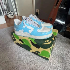 BAPE STA sneakers i blått och vitt - Säljer ett par BAPE STA sneakers i blått och vitt med klassisk stjärndesign på sidan. Skorna har vit sula, blå detaljer och snörning. Perfekta för dig som gillar streetwear och vill sticka ut med en ikonisk modell.