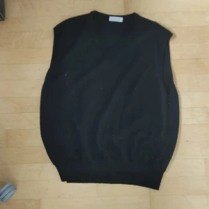 Svart ullväst från Gran Sasso - Snygg svart väst från Gran Sasso i mjukt ullmaterial. Den har en klassisk v-ringad design som passar perfekt för lager-på-lager-stil. Tillverkad i Italien, vilket garanterar hög kvalitet och stil. Perfekt för att hålla värmen med stil under kyligare dagar. Bra skick . Öppen mot bud