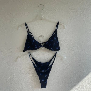 Svart bikini med fjärilsmönster - Svart bikini med små blå fjärilar. Bikinin har trekantsformad överdel med smala axelband och matchande nederdel. 