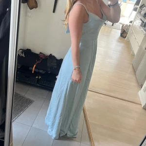 Ljusgrön balklänning - Säljer en elegant ljusgrön långklänning med smala axelband och figurnära passform upptill. Klänningen har en mjuk, svepande kjol och v-ringad urringning. Perfekt inför balen! Helt oanvänd med prislappen kvar