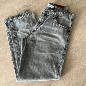 Grå jeans från Woodbird - Säljer ett par grå jeans från Woodbird i klassisk femficksmodell. Jeansen har normal passform och raka ben, tillverkade i bomull. Snyggt läderpatch bak i midjan och diskret logga vid bakfickan. Storkek 30-31. 