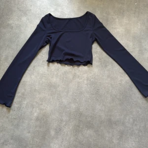 Mörkblå croppad långärmad topp - Säljer en mörkblå croppad topp med långa ärmar och vågig kant nertill. Toppen har en fyrkantig ringning och är tillverkad i ett stretchigt material. Perfekt att styla med höga jeans eller kjol.