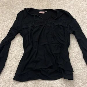 Svart långärmad topp med spets från KappAhl - Säljer en svart långärmad topp från KappAhl i storlek 38. Toppen har fina spetsdetaljer.
