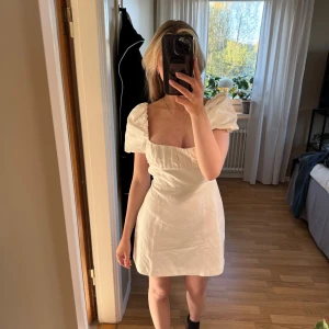 Vit kortklänning/studentklänning - Superfin vit kortklänning från Zara med puffärmar och öppen rygg med snörningsdetaljer. Klänningen har en figurnära passform och knytning i ryggen som ger en unik look. 