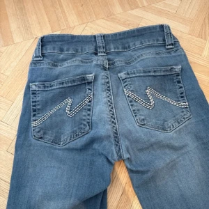 Blå bootcut jeans med broderade bakfickor - Snygga blå jeans med bootcut passform och broderade detaljer på bakfickorna. Klassisk femficksmodell med normal midja och dragkedja framtill. Perfekta för en avslappnad och trendig look.