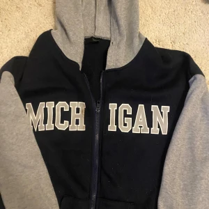 Blå och grå hoodie med MICHIGAN-tryck från SHEIN - Mysig hoodie från SHEIN i mörkblått med grå ärmar och huva. Stor vit MICHIGAN-text framtill och dragkedja. Perfekt för en avslappnad stil och enkel att matcha med jeans eller leggings.