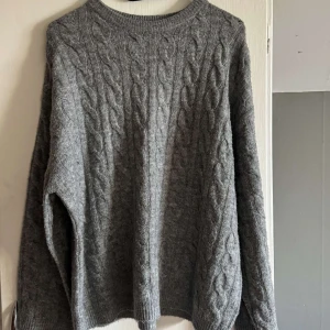 Grå kabelstickad tröja - Mysig grå kabelstickad tröja med rund halsringning och långa ärmar. 