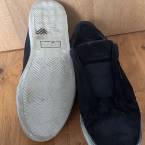 Svarta slip-on sneakers från Axel Arigato - Svarta slip-on sneakers från Axel Arigato med ovandel i mocka och vit platt sula. Skorna har elastisk panel över vristen och minimalistisk design med diskret logga på sidan. Box ingår jag säljer dem men det är min väns 😌