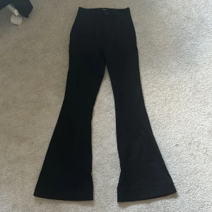 Svarta bootcut kostymbyxor från Object - Svarta kostymbyxor från Object med bootcut-passform och hög midja. Byxorna har bälteshällor, knapp och dragkedja framtill samt fickor bak. Perfekta för en stilren och trendig look.