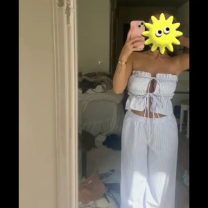 Blå- och vitrandig byxa med bandeau-topp - Säljer en somrig outfit ljus blå/lila som jag råka beställa två stycken av. Bandeau-toppen knyter du fast där framme i rosetter, hur löst eller tajt du vill den ska sitta. Väldigt luftigt och skönt till sommaren. 