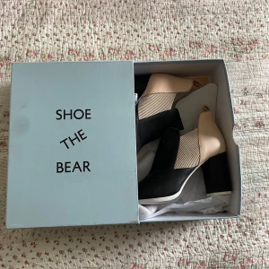 Shoe The Bear boots med klack - Snygga boots från Shoe The Bear i modellen Elise L. Skorna har en mix av svart och beige färg, hög klack och rund tå. Tillverkade i skinn med ribbade detaljer på sidan. Perfekta för dig som vill ha något unikt och stilrent. (De är min kamera som är sönder därför kan de se ut att de är en fläck)