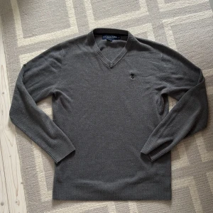  v-ringad U.S. Polo Assn tröja  - Säljer en stilren grå v-ringad tröja från U.S. Polo Assn. Tröjan har långa ärmar, ribbade muddar och en liten broderad logga på bröstet. Perfekt för lager-på-lager och enkel att matcha med det mesta.