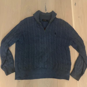 Blå cable knit half zip från Ralph Lauren - Säljer en blå stickad tröja från Polo Ralph Lauren med halv dragkedja och kabelstickat mönster. Tröjan har hög krage och långa ärmar, perfekt för kyligare dagar. Klassisk logga broderad på bröstet. Skriv om ni har frågor eller vill ha fler bilder!