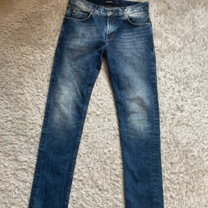 Blå jeans från J.Lindeberg - Snygga blå jeans från J.Lindeberg med klassisk femficksdesign och dragkedja. Jeansen har en straight passform och är tillverkade i denim med lätt slitning framtill och baktill för en cool look. W30 L34