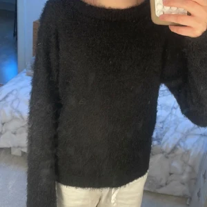 Svart fluffig stickad tröja från 157 - Mysig svart stickad tröja från 157 med fluffig textur. Tröjan har rund halsringning och långa ärmar, perfekt för kyligare dagar. Enkel och stilren design som passar till mycket. Storleken är 130 men den är nästan förstor på mig som har storlek 150.