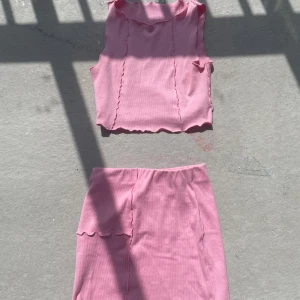 Rosa ribbad kjol med tillhörande linne - Supersöt rosa kjol i ribbat material med tillhörande linne. Kjolen har en rak passform och är kort, perfekt för en trendig look. Matchande top för en komplett outfit! Ifrån Nly Trend